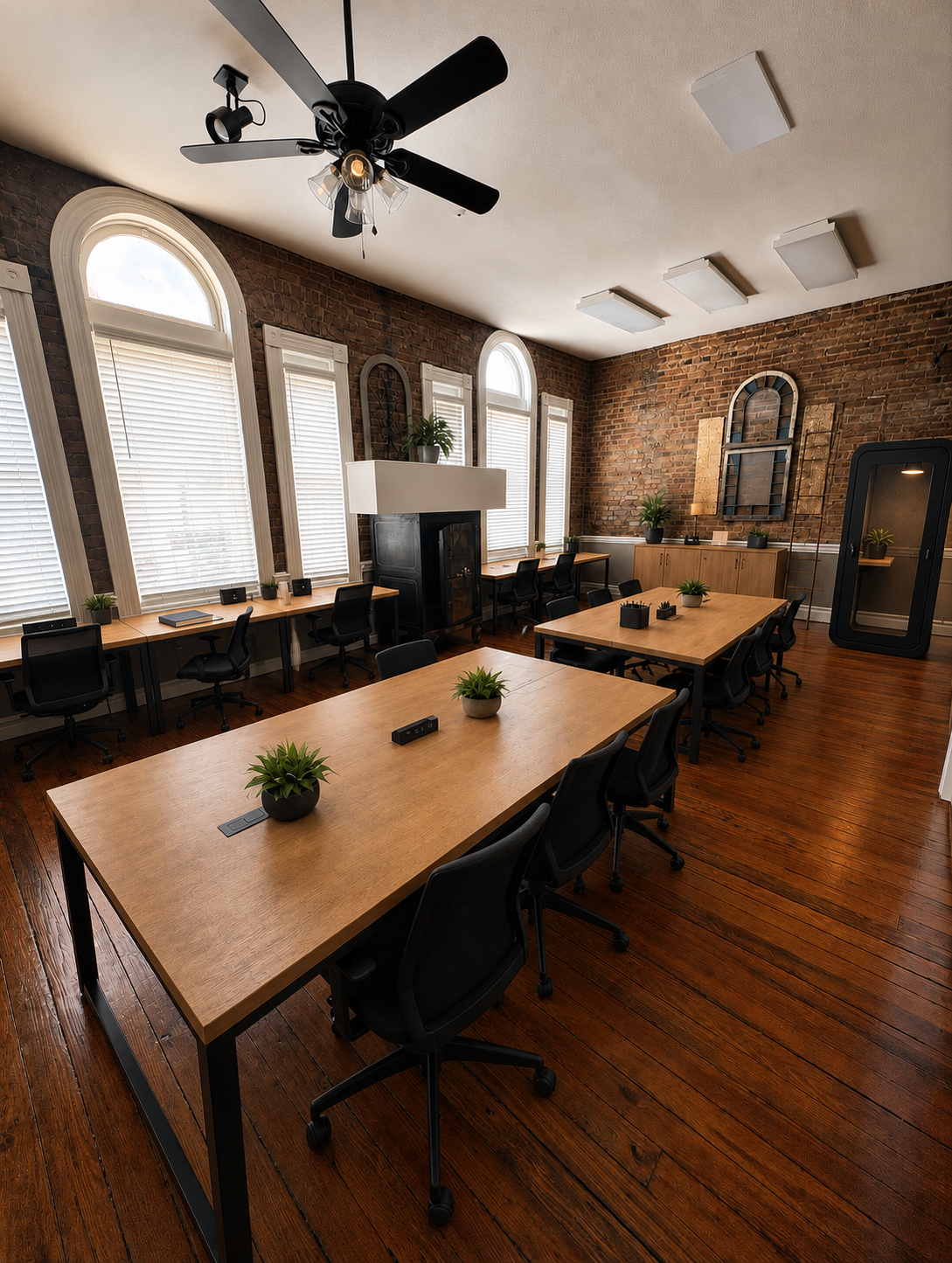 A warm historic brick workspace with shared wood tables, desks, and quiet phone rooms